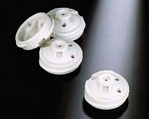 The image shows a set of four white plastic buttons on a black surface. The buttons are arranged in a triangular formation, with the largest button in the center and two smaller buttons on either side