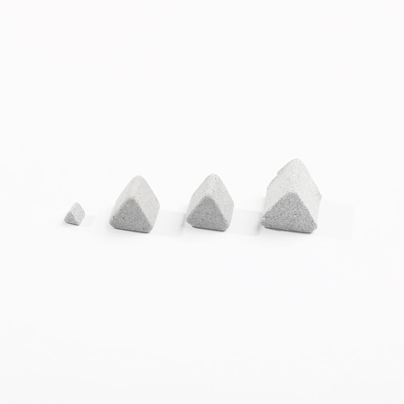 The image shows a set of four grey concrete pyramids on a white background. The pyramids are arranged in a triangular formation, with the largest one in the center and two smaller ones on either side.