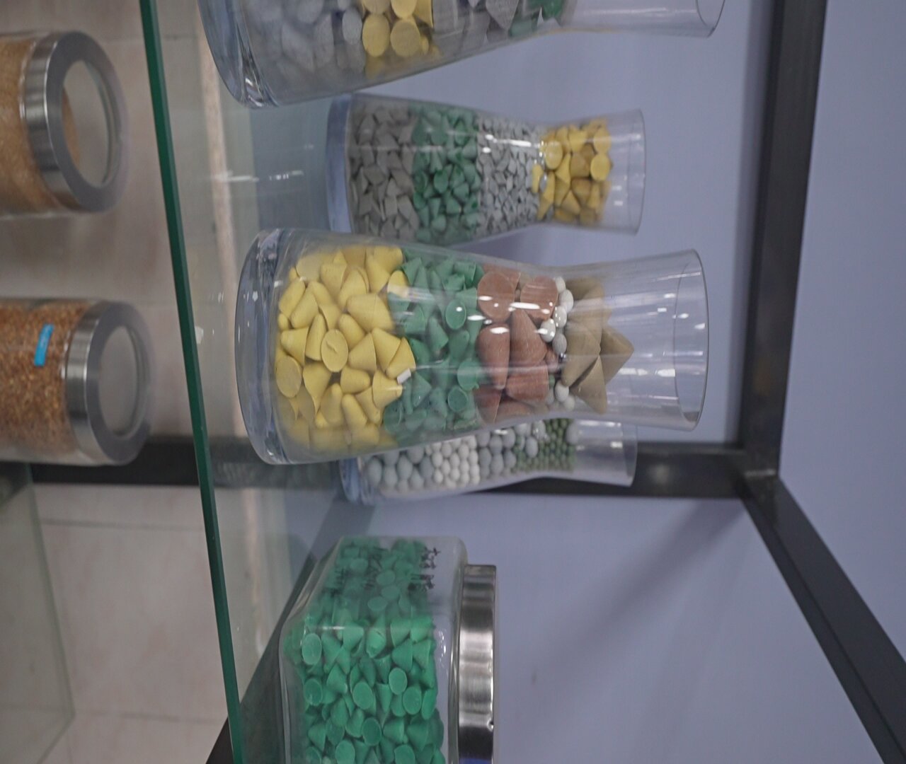 Frascos transparentes con muestras de medios de distintos colores y formas: conos amarillos, triángulos verdes, cilindros marrones y blancos